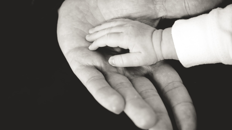 Aikuisen ja vauvan kädet mustavalkokuvassa